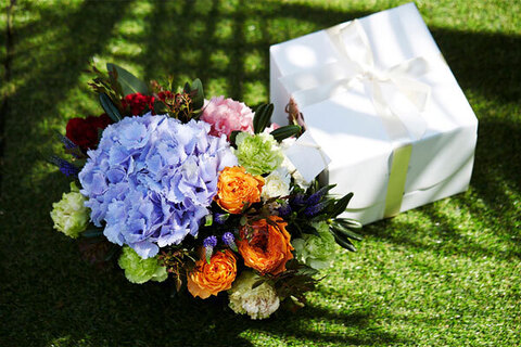 Square white box on a lawn with a bouquet of colorful flowers beside it