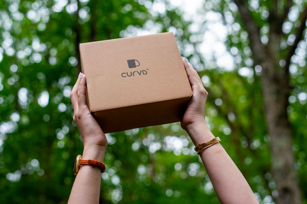 A cardboard box held aloft with two hands against a background of trees