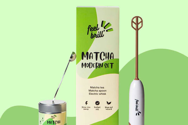 Set di prodotti Feel Brill su sfondo verde: tè matcha, cucchiaino e miscelatore elettrico.